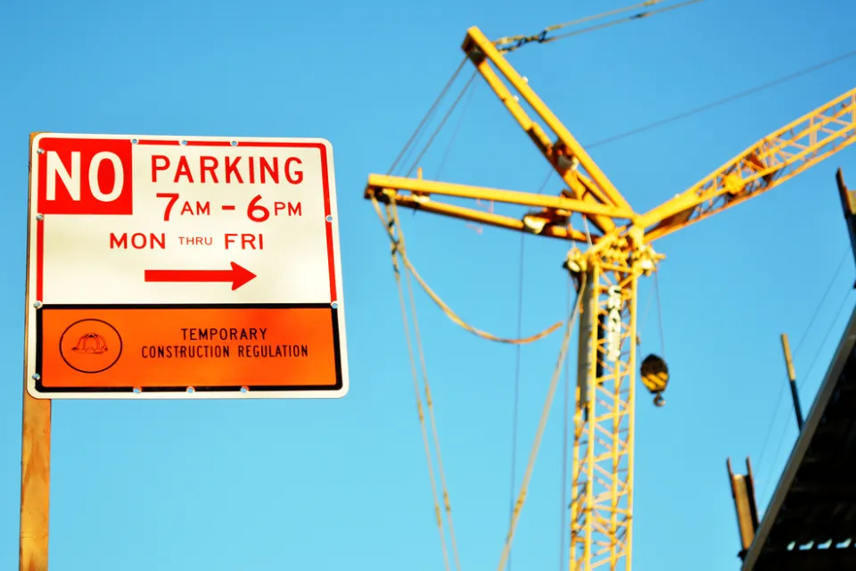 A sign reads “No Parking” for temporary construction, with a construction crane in the background.